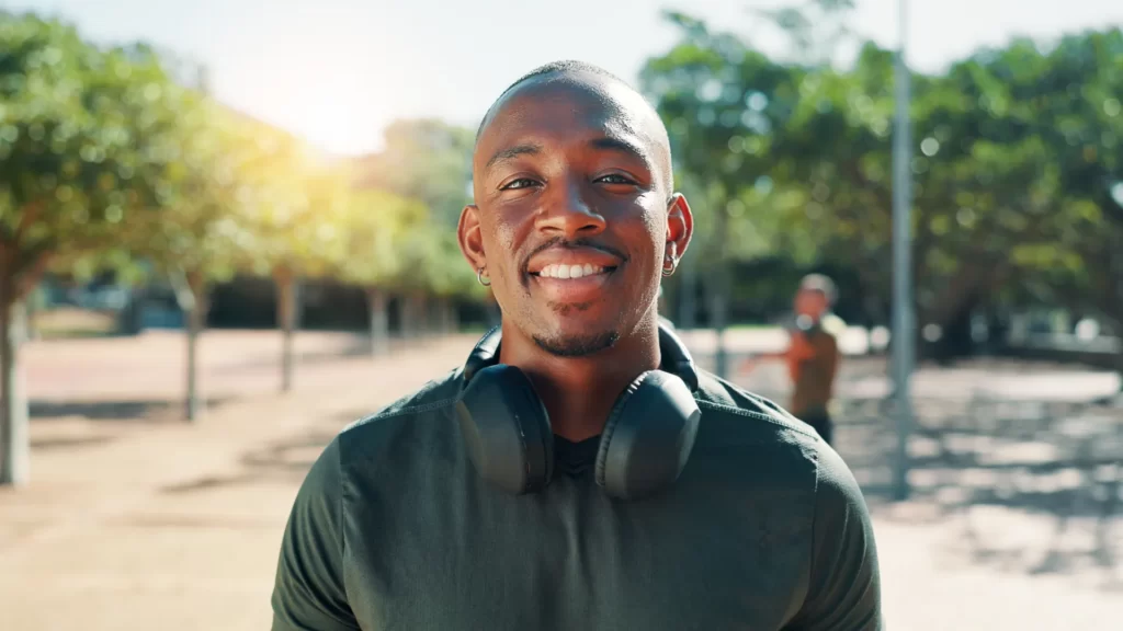 smiling man with headphones in sunny green park utc